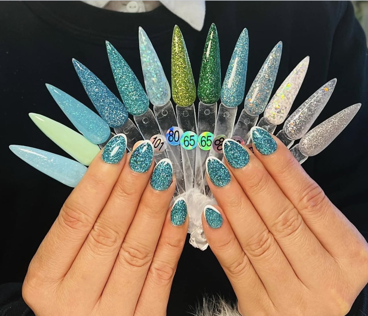Twee handen met turquoise glitternagels voor een waaier met kleurstalen